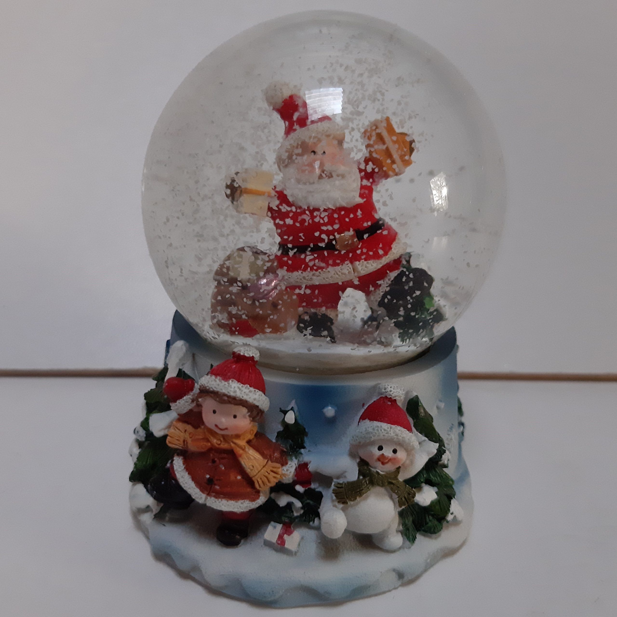 Sneeuwbol kerstman met zak cadeaus op blauwe basis met kerstkind en sneeuwpop 9cm